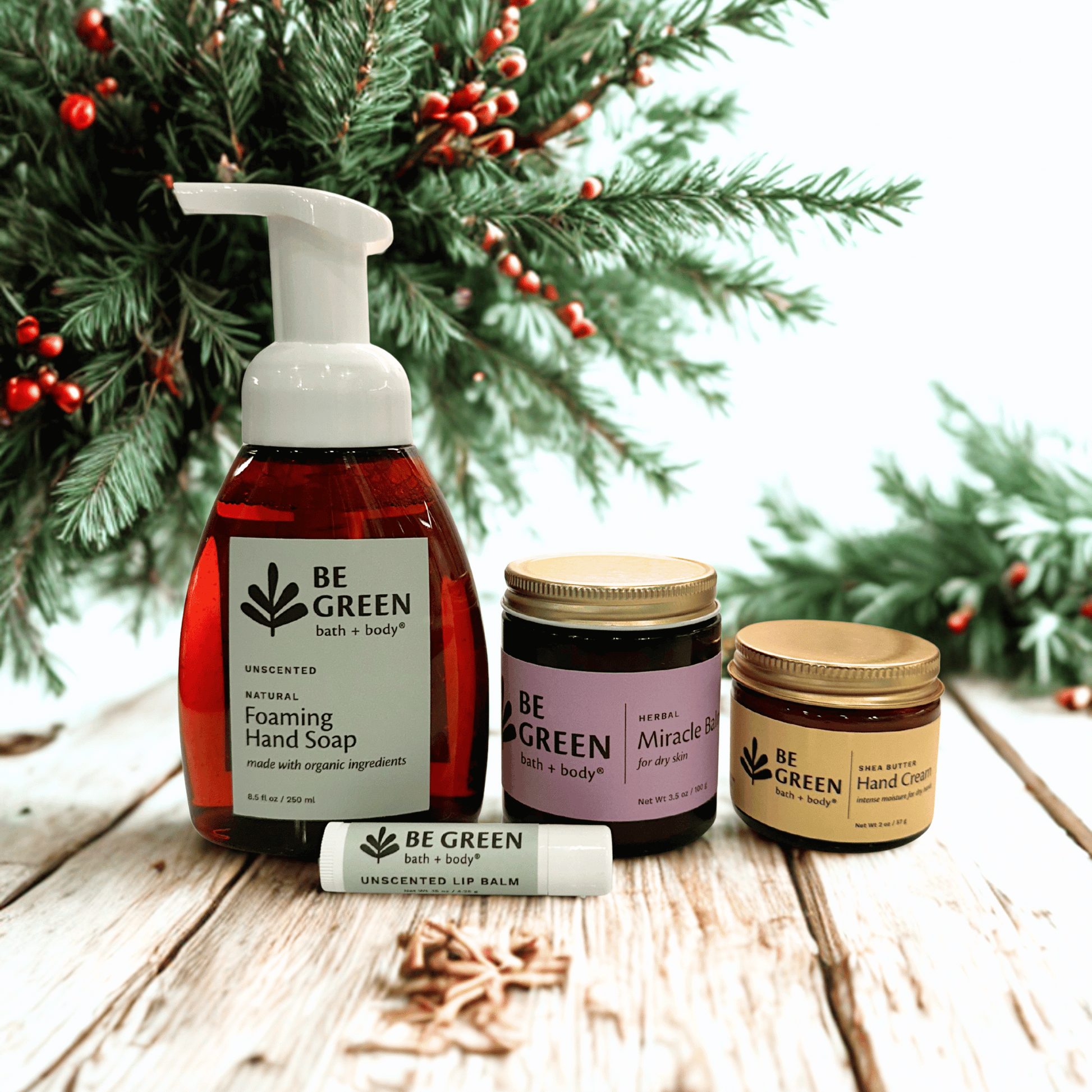 Be Green bath & body products including foaming hand soap, lip balm, and creams on a wooden surface with Christmas decorations.