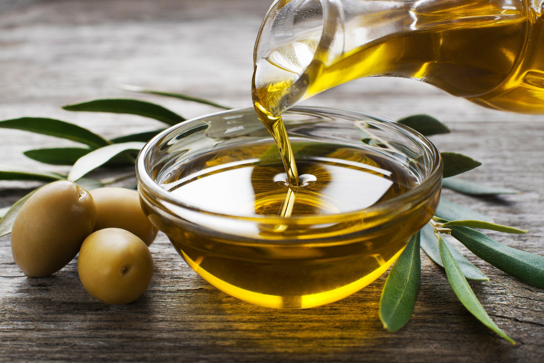 Picture of olive oil in clear bowl with olives and leaves