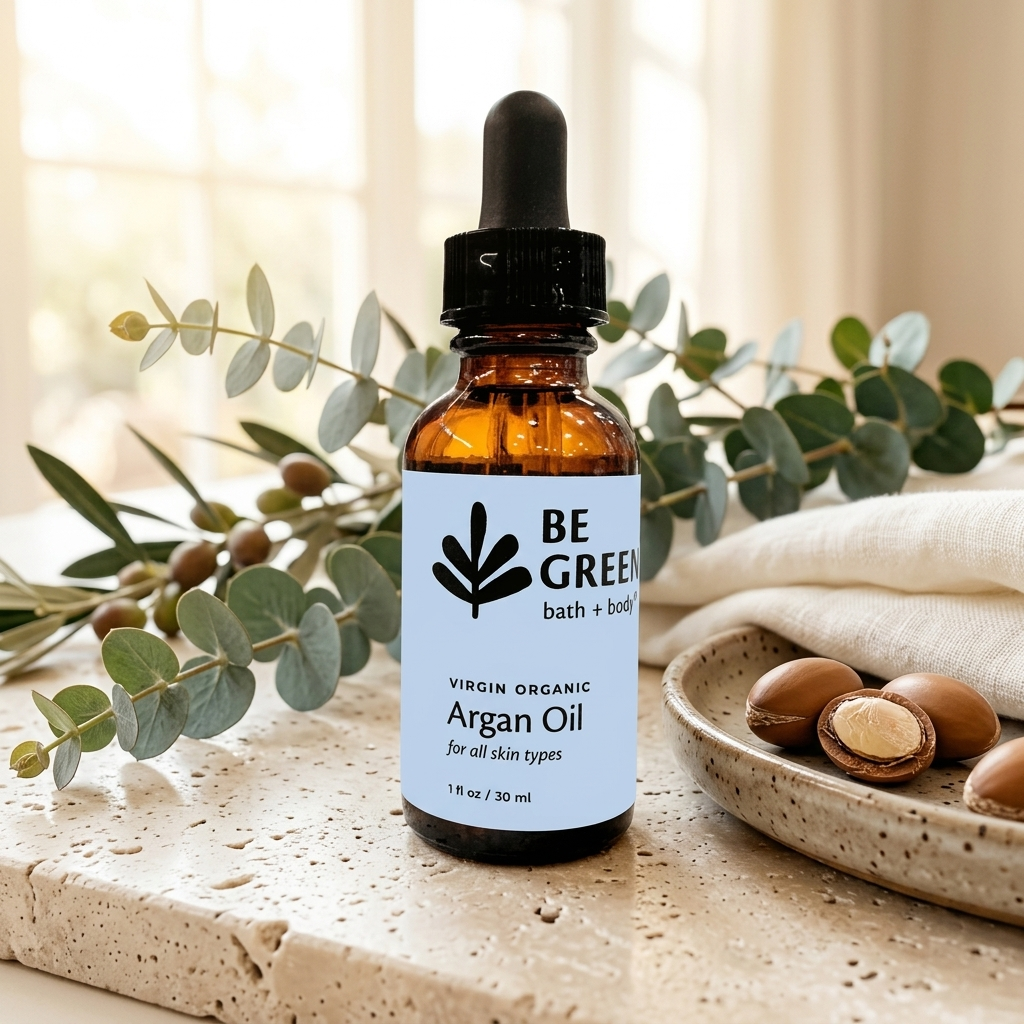 An amber glass dropper bottle of BE GREEN Virgin Organic Argan Oil stands on a stone surface with eucalyptus branches and a dish of argan nuts in a softly lit indoor setting.