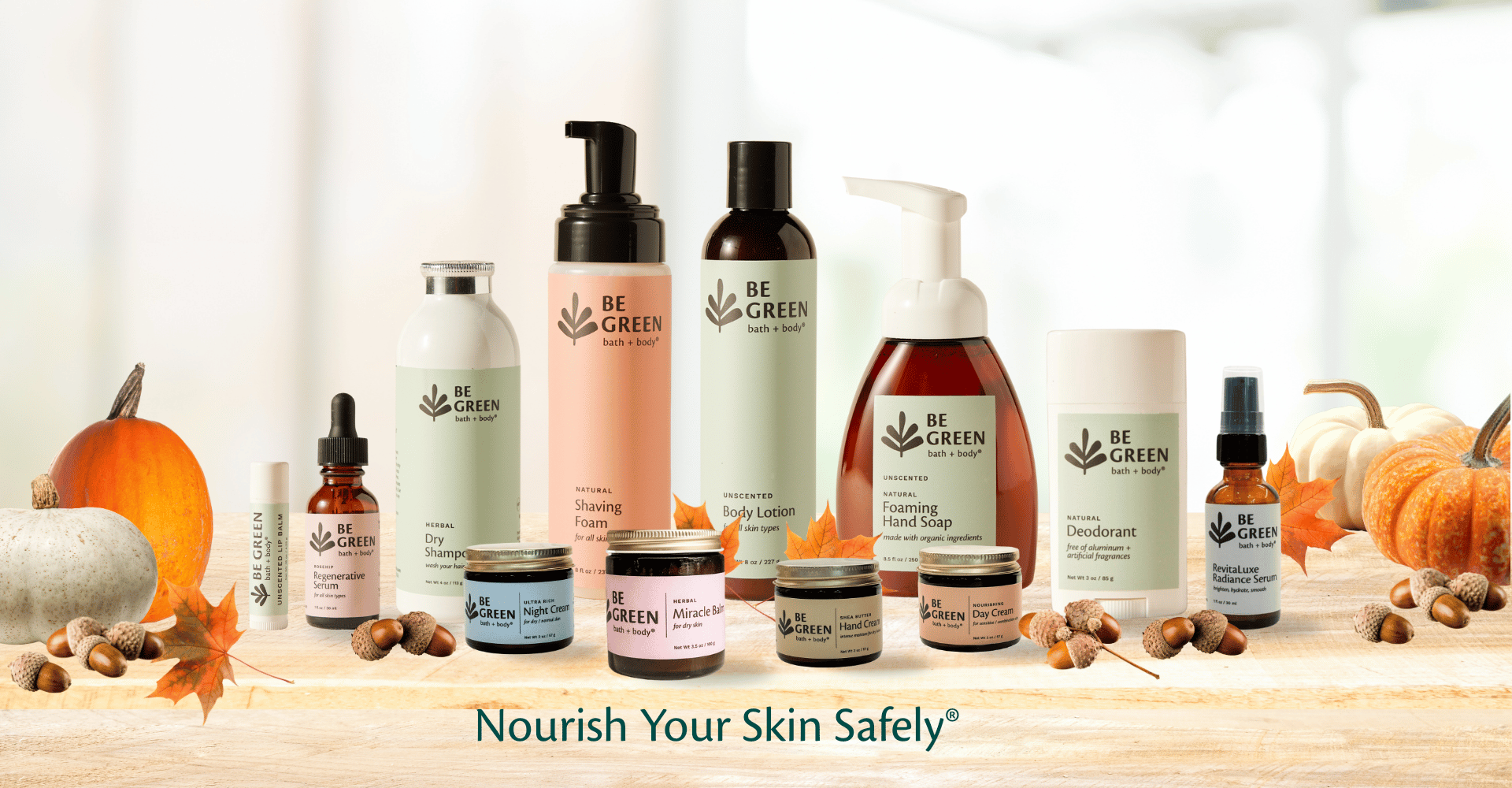 Collection of 'Be Green' skincare products on a wooden surface with pumpkins and leaves.