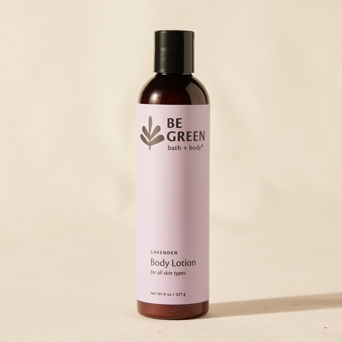 A bottle of BE GREEN bath and body lavender body lotion, featuring a light lavender label and a black cap, set against a warm beige background.