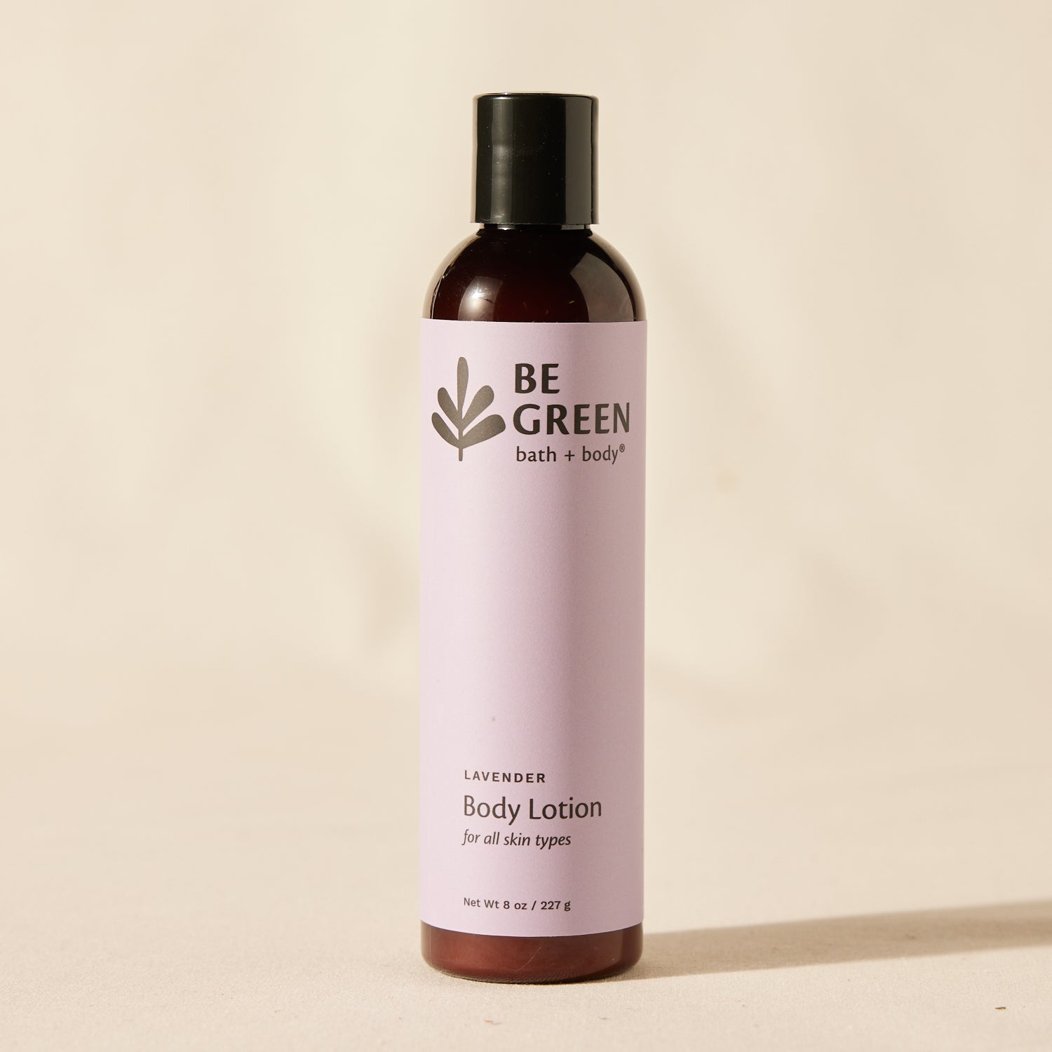 A bottle of BE GREEN bath and body lavender body lotion, featuring a light lavender label and a black cap, set against a warm beige background.