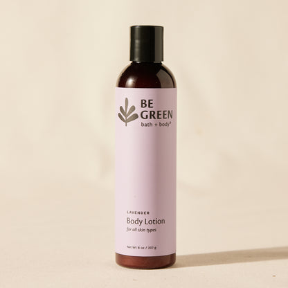 A bottle of BE GREEN bath and body lavender body lotion, featuring a light lavender label and a black cap, set against a warm beige background.