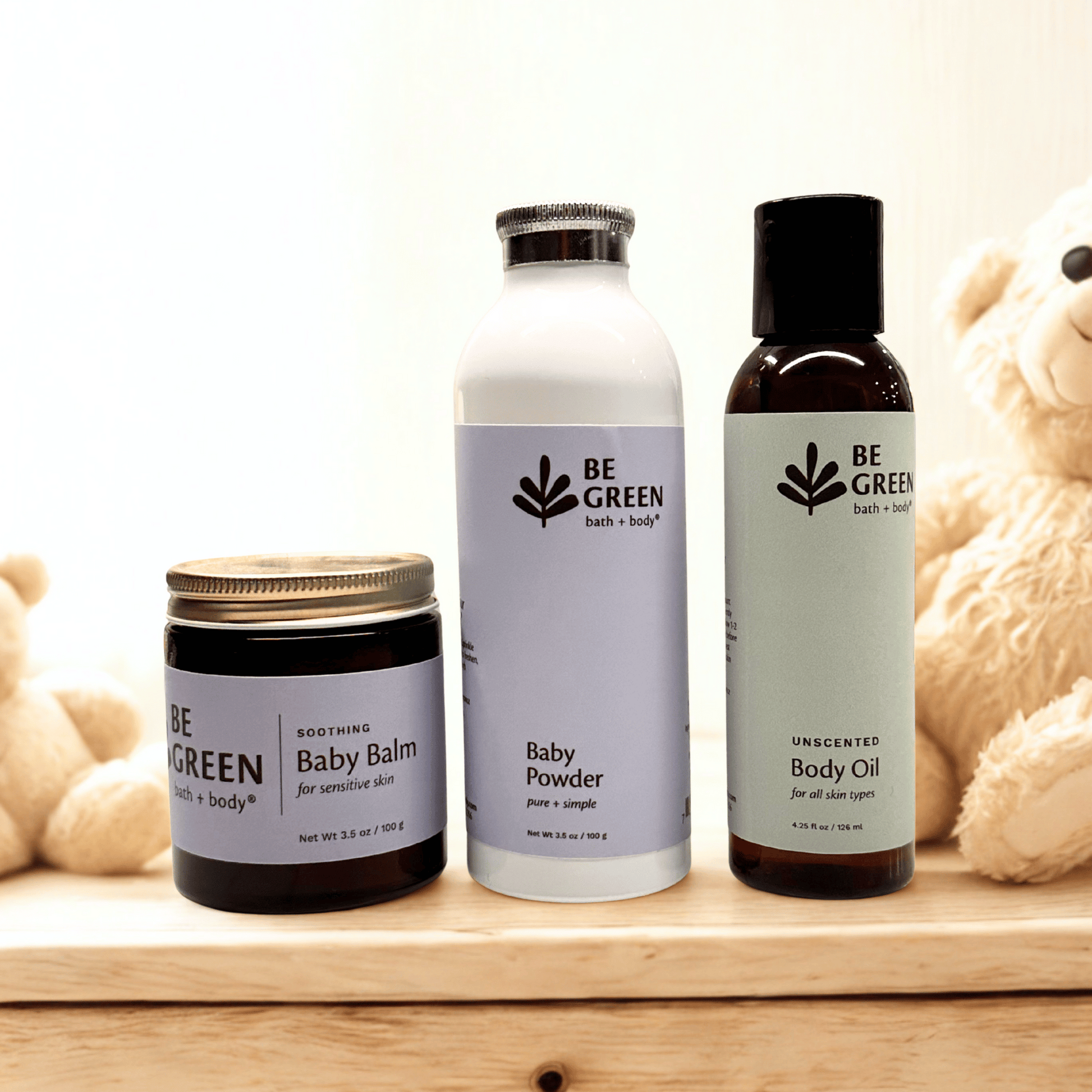 Set of 'Be Green' baby care products including balm, powder, and body oil on a wooden surface.