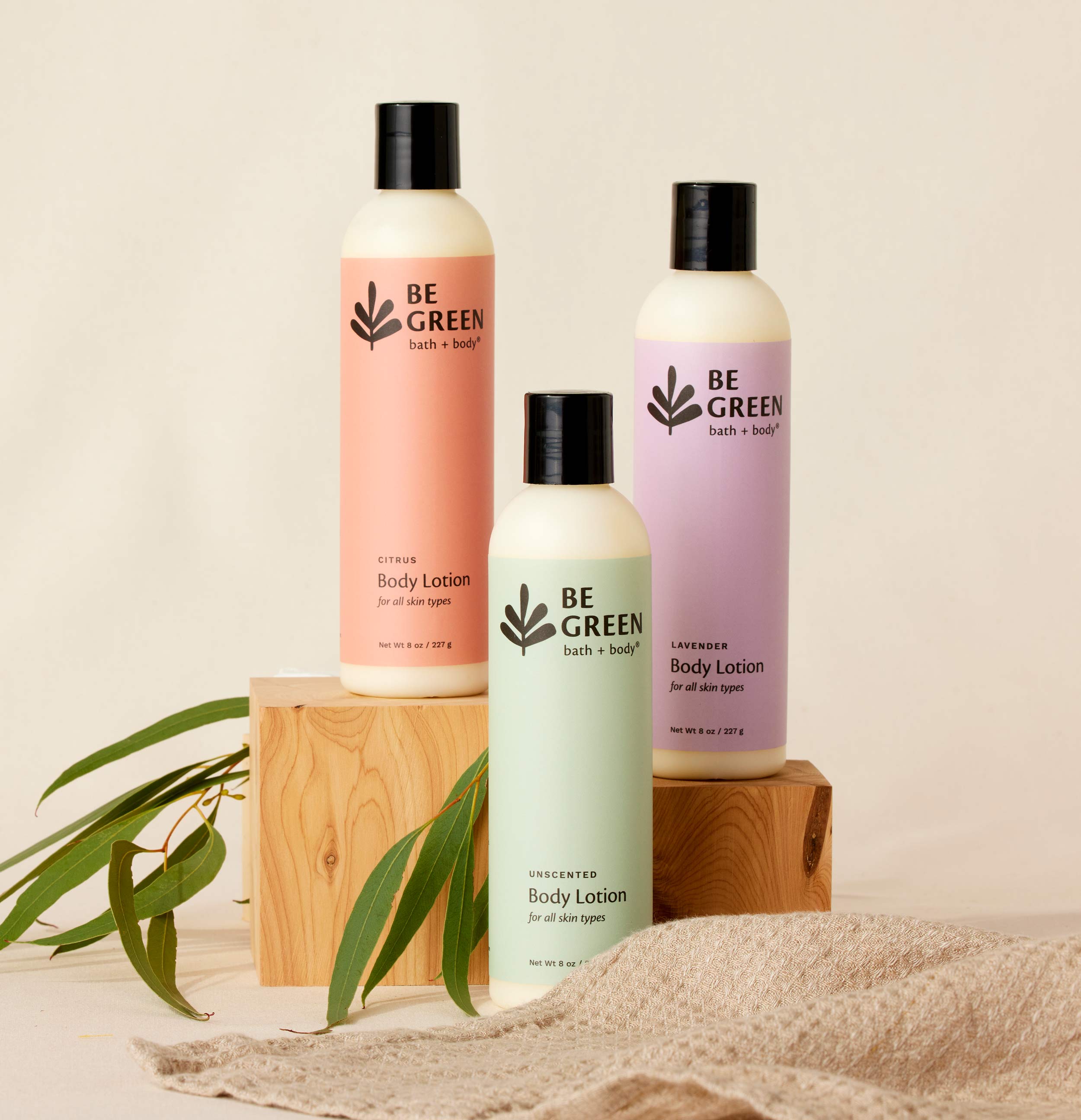 Picture of three lotion bottles on wood risers with green leaves.