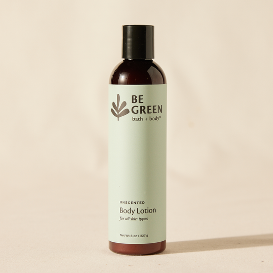 A bottle of BE GREEN bath + body unscented body lotion, featuring a pale sage green label and a dark brown bottle with a black cap, set against a warm beige background.