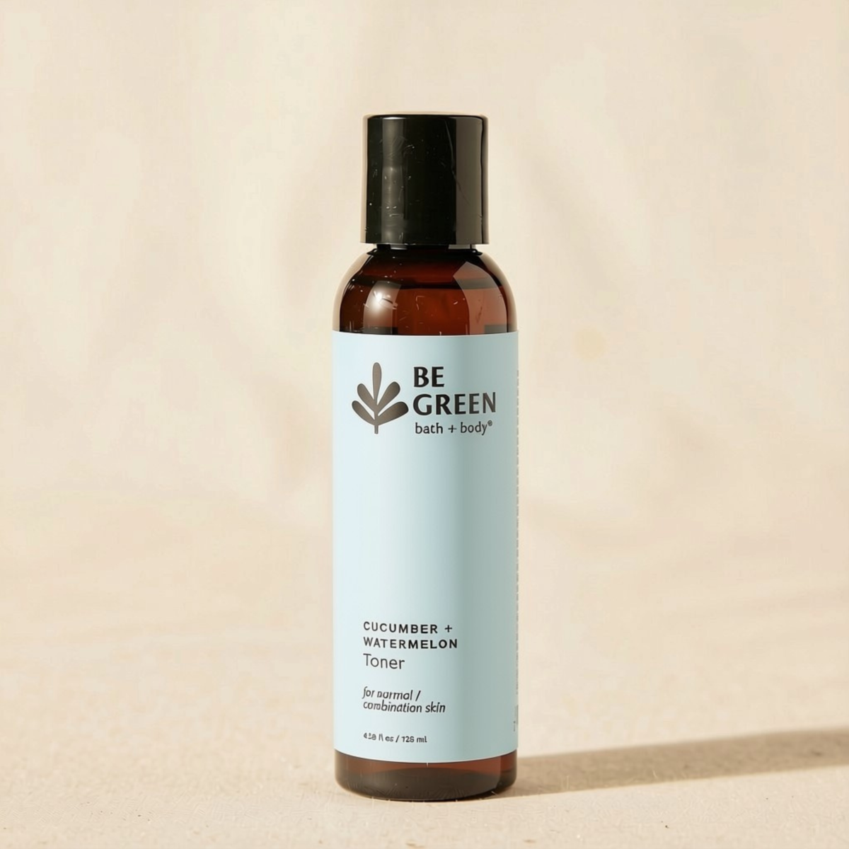 A bottle of BE GREEN Cucumber + Watermelon Toner with a light blue label and black cap, standing on a beige textured surface.