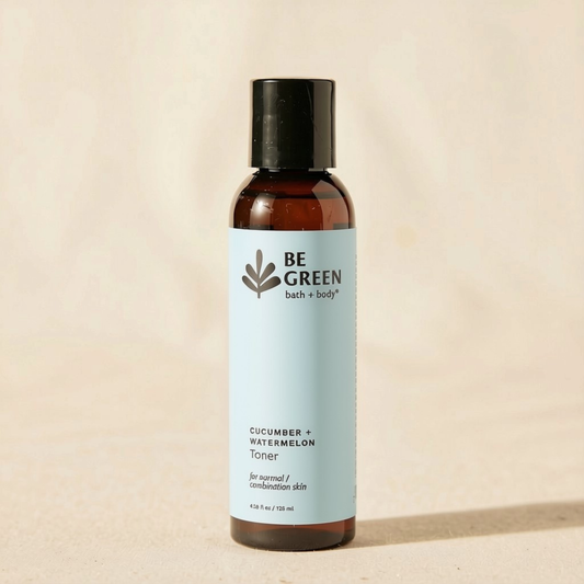 A bottle of BE GREEN Cucumber + Watermelon Toner with a light blue label and black cap, standing on a beige textured surface.