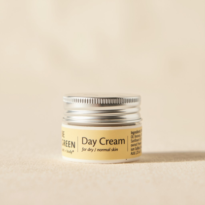 A trial size jar of Day Cream dry  featuring a light yellow label and a silver metal screw cap, set against a matching beige background.