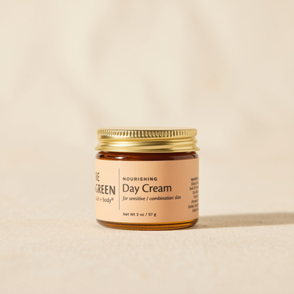 A small amber glass jar of Be Green Day Cream with a gold metal lid and a beige label, set against a warm beige background.