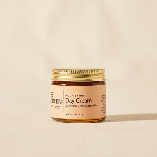 A small amber glass jar of Be Green Day Cream with a gold metal lid and a beige label, set against a warm beige background.