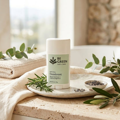A deodorant stick bottle sits on a stone tray with herbs and a small dish of lavender, styled on a beige towel near a window.