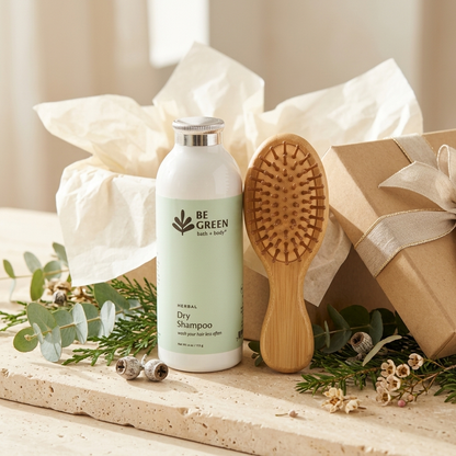 Bottle of Dry Shampoo and bamboo brush on a light stone with greenery and a gift box.