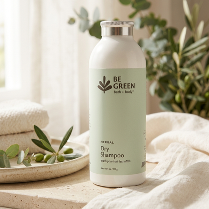 A bottle of BE GREEN Herbal Dry Shampoo stands on a light stone surface with soft beige fabric and greenery in the background.
