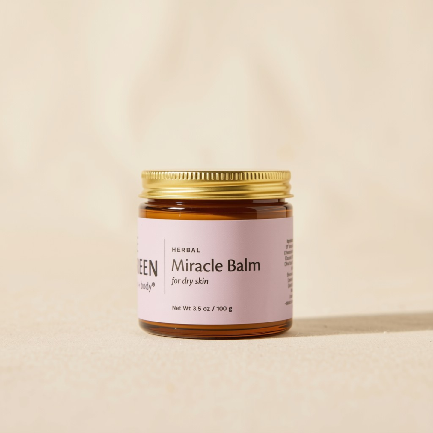 A small amber glass jar of Herbal Miracle Balm with a gold metal lid and a light pink label, set against a warm beige background.