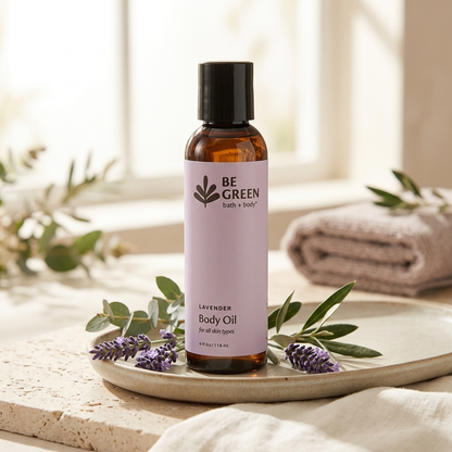 A bottle of BE GREEN Lavender Body Oil stands on a ceramic tray with lavender sprigs and greenery, set in a softly lit spa-like scene with a towel and window in the background.