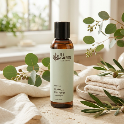 A bottle of BE GREEN Gentle Makeup Remover cleansing oil, styled on a stone surface with white towels and eucalyptus branches in a bright, natural setting.