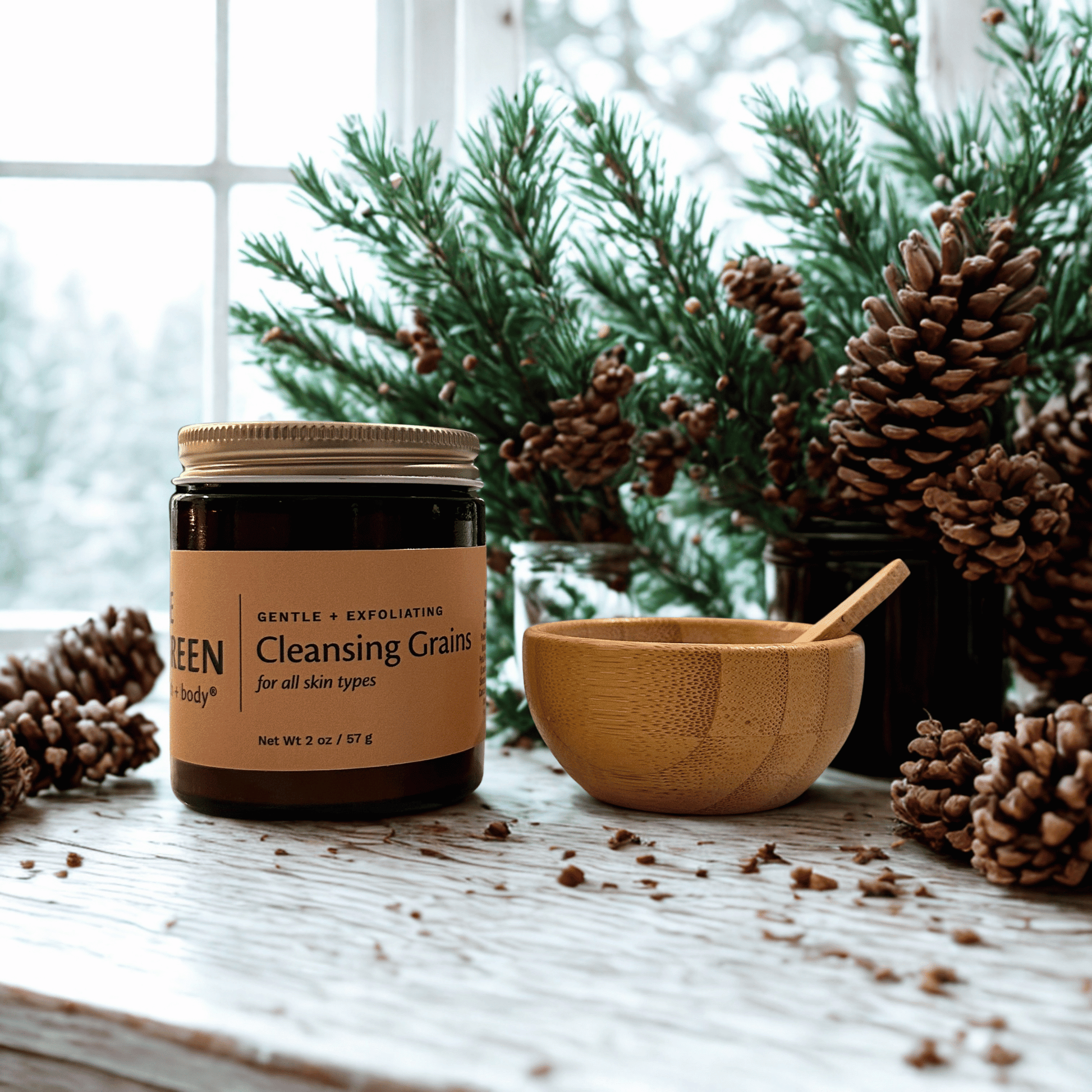 Jar of 'Cleansing Grains' with a wooden bowl and spoon on a wooden surface with pinecones and a snowy window background.