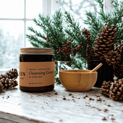 Jar of 'Cleansing Grains' with a wooden bowl and spoon on a wooden surface with pinecones and a snowy window background.