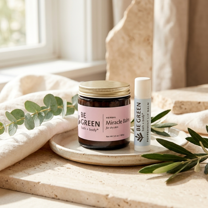 Miracle Balm and Lip balm on a light tray and stone with greenery