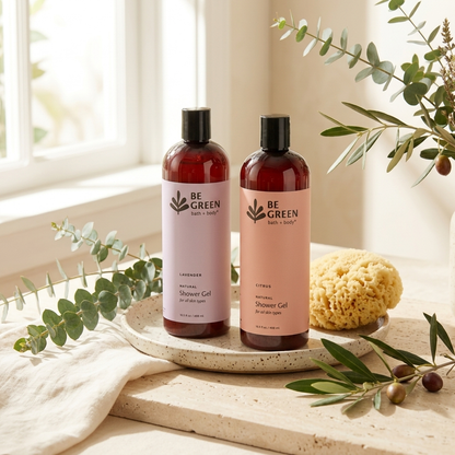Two amber plastic bottles of BE GREEN body wash, one labeled Lavender and one labeled Citrus, standing on a round stone tray with a sponge and eucalyptus branches in a bright, natural setting.