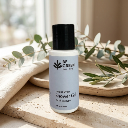A bottle of BE GREEN bath and body Unscented Shower Gel stands on a stone surface with a folded beige towel and eucalyptus branches in the background.