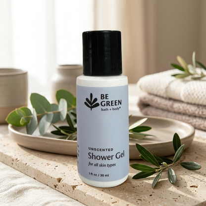 A bottle of BE GREEN Unscented Shower Gel placed on a stone tray with eucalyptus leaves and folded towels in the background, creating a spa-like setting.